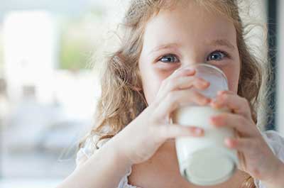 A young girl with curly blonde hair drinking milk from a glass