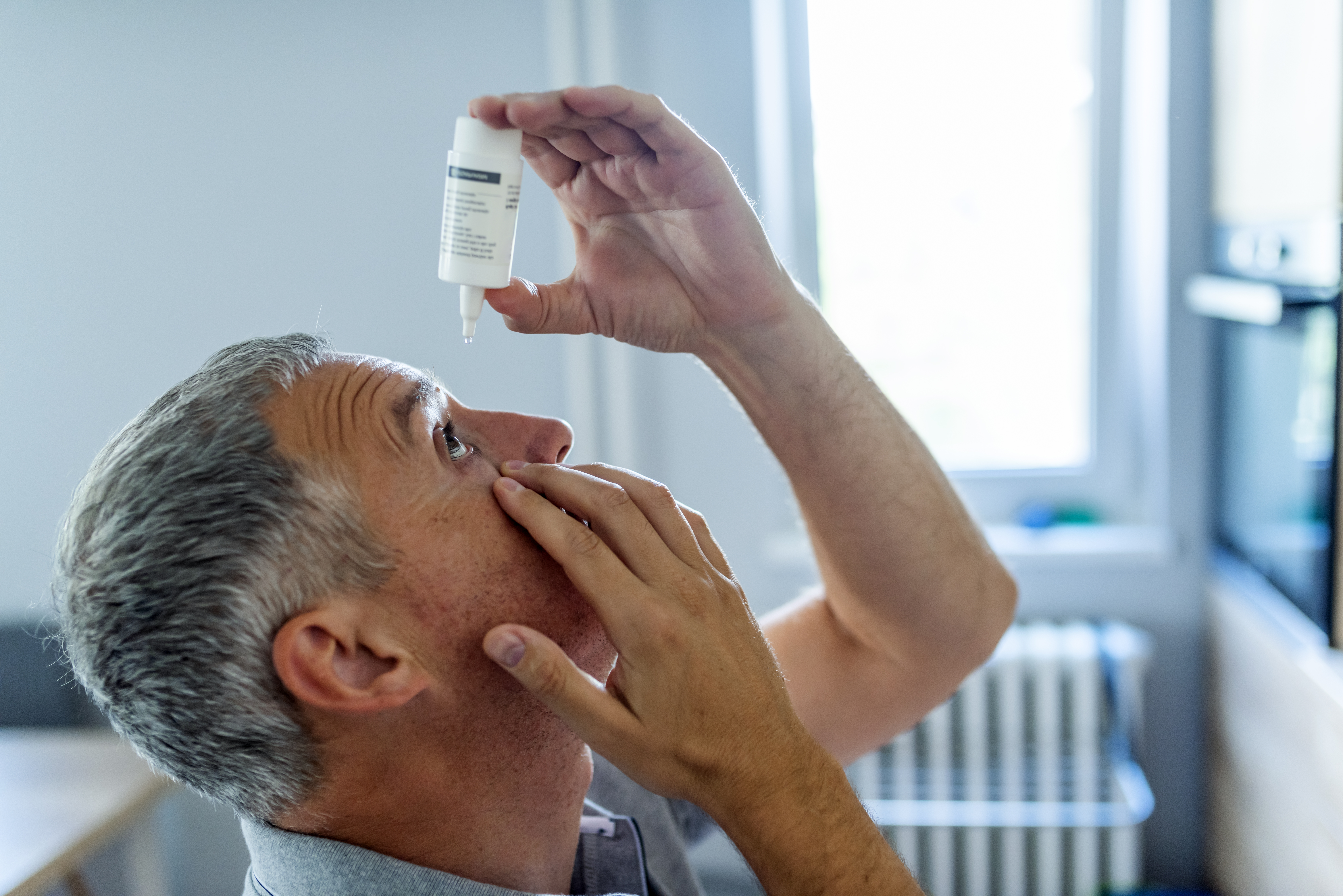 man putting drops in eyes