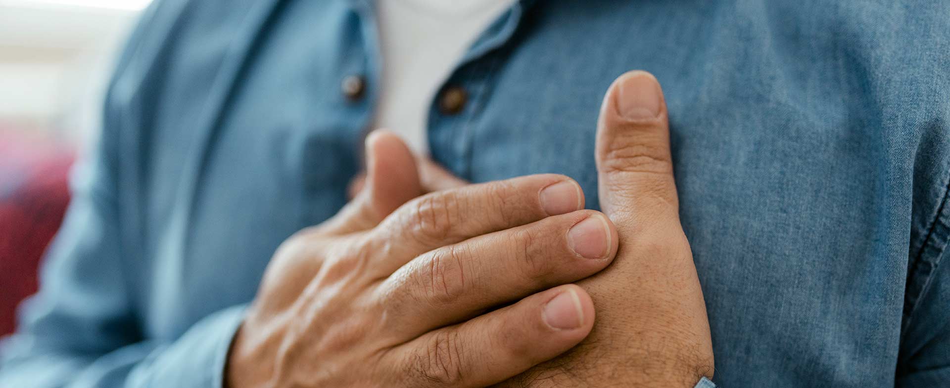 A closeup of man in a denim shirt holding both hands over his heart. coronary calcium scan