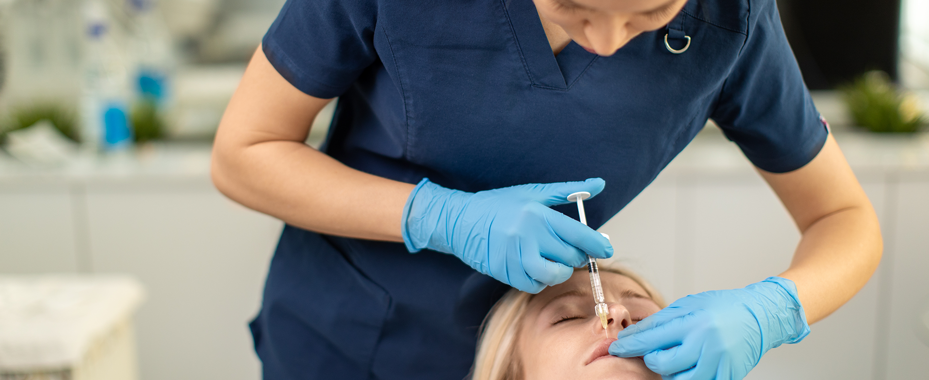 Woman laying back with her eyes closed. She has blonde shoulder-length hair and is getting dermal filler injected into her upper lip. dummy desktop Image