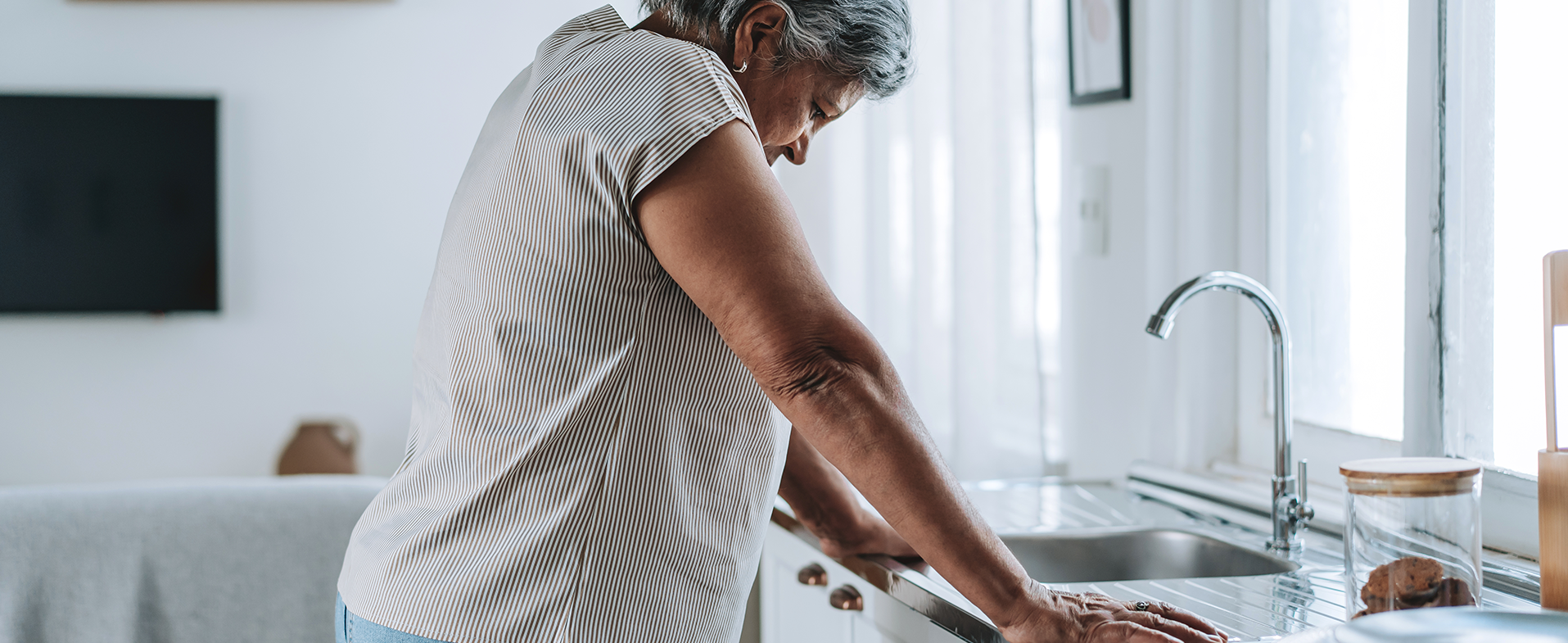Older woman leaning over sink looking tired wearing beige T-shirt. woman with brain fog