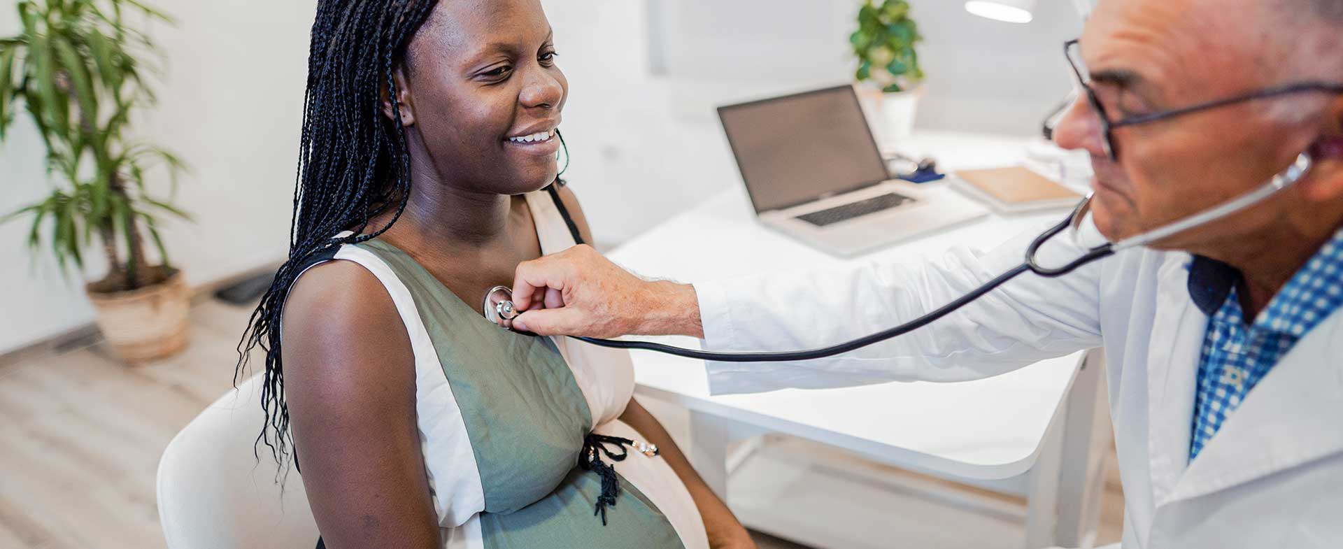 A pregnant woman sits while a male doctor uses a stethoscope to listen to her heart. pregnancy heart changes