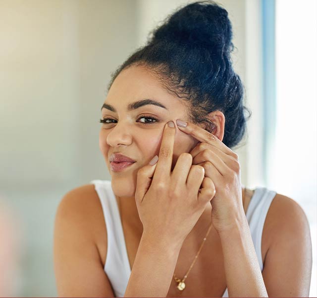 woman looking at acne in mirror