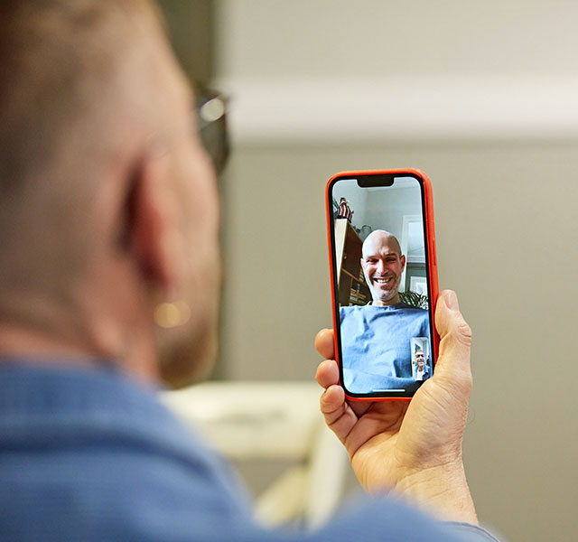 A person is using a smartphone to video call another person, whose image is visible on the screen. The person on the screen is smiling. real digital connections