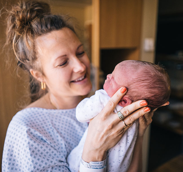 A woman in a hospital gown happily holding up her newborn baby. postpartum checklist