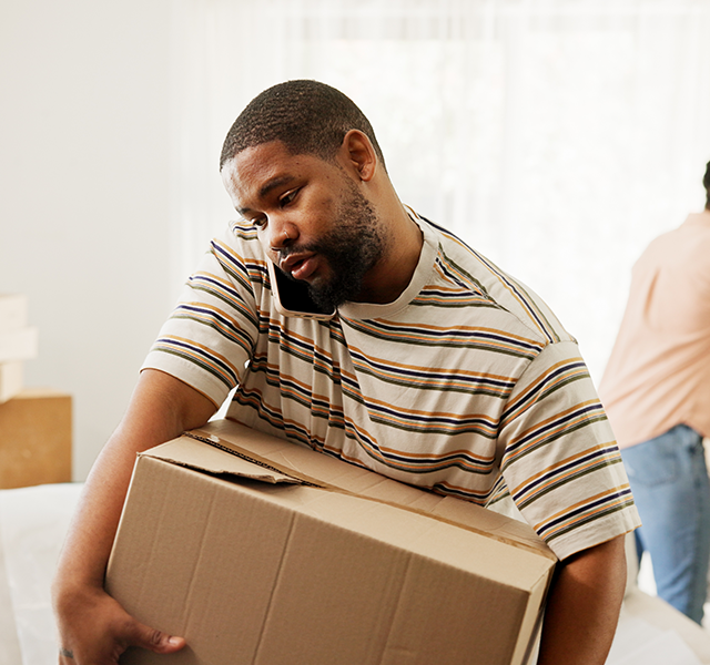Man wearing a striped t-shirt and carrying a box while talking on the phone on moving day. dummy mobile image