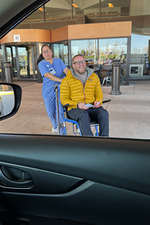 vascular patient Eric getting wheeled in a wheelchair to his car after surgery
